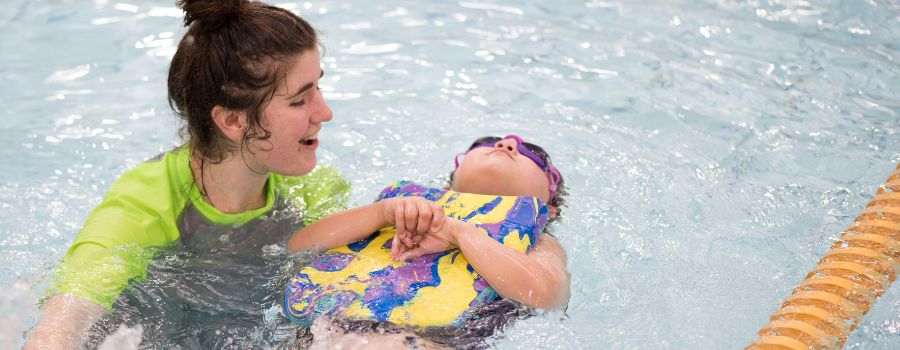 Swim coach with a child in the pool with a board