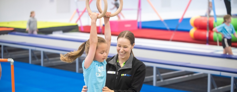 gymnastics coach teaching child to use the rings in a gymnastics stadium