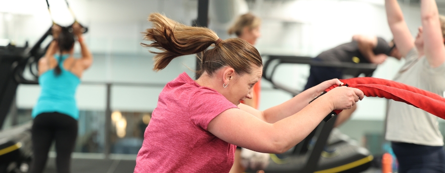 in the foreground, a person uses the ropes as the rest of the group fitness class uses other equipment around her