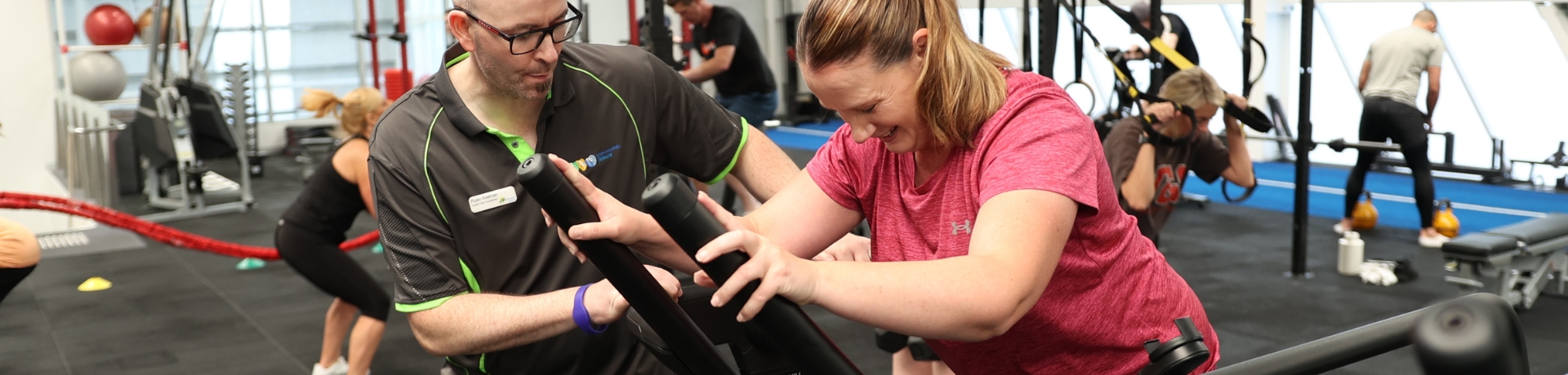 Group of people working out on a variety of gym equipment overseen by a coach