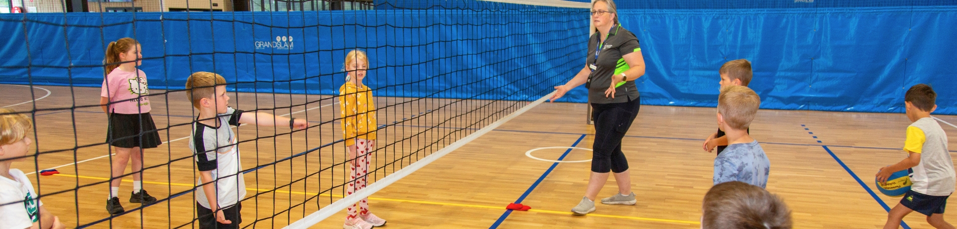 Kids on a volleyball court being instructed by a coach