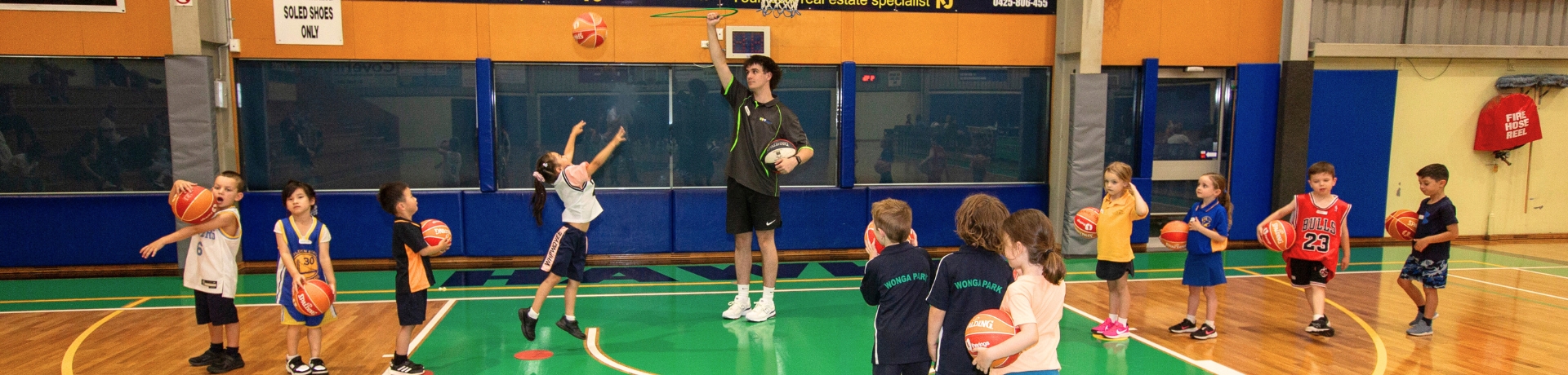 Children line up to throw a basketball through a hoop on an indoor basketball court