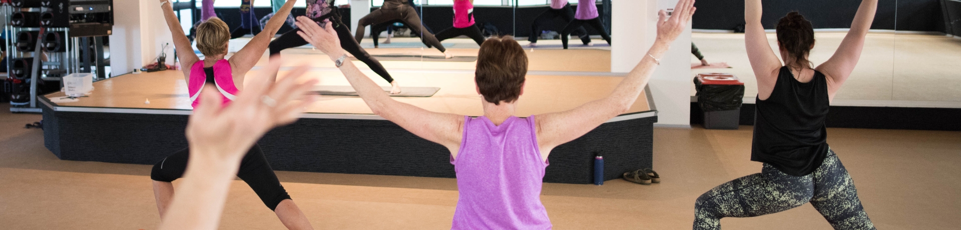 a group of people in a standing yoga pose with arms up facing a mirror